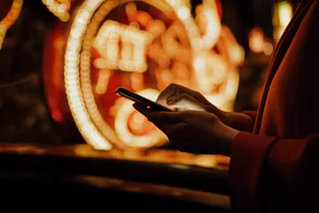 A cheerful woman in traditional clothing using her smartphone during a festive moment, showing how easily the KWIKIBET app fits into everyday life.